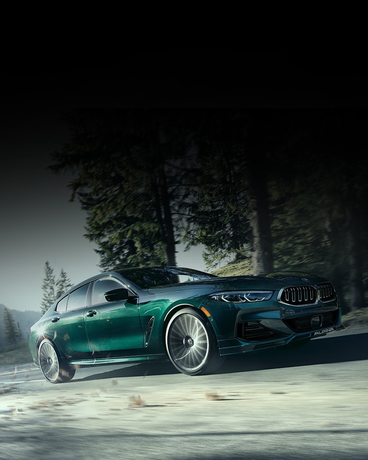 A 2025 ALPINA B8 Gran Coupe drives along a woodland road
