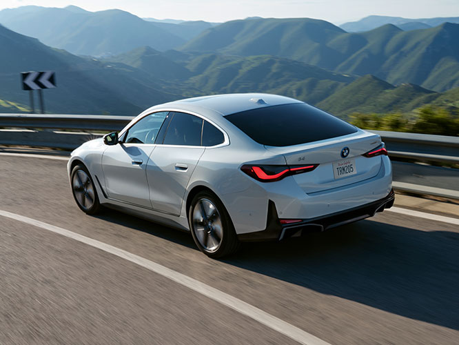 A BMW i4 Gran Coupe accelerates around a corner while driving through a mountain range