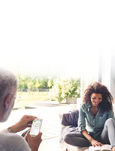 Woman on couch reading a book with a man looking at smartphone screen