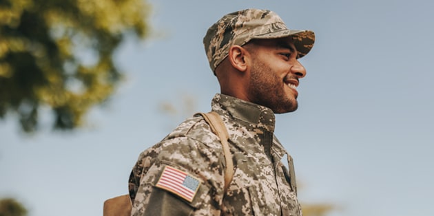 A smiling military member in uniform stands in front of a clear sky