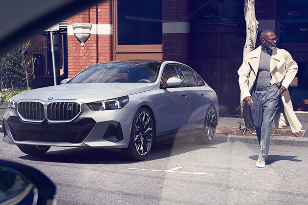 A snazzy BMW driver in a trenchcoat walks away from his parked BMW