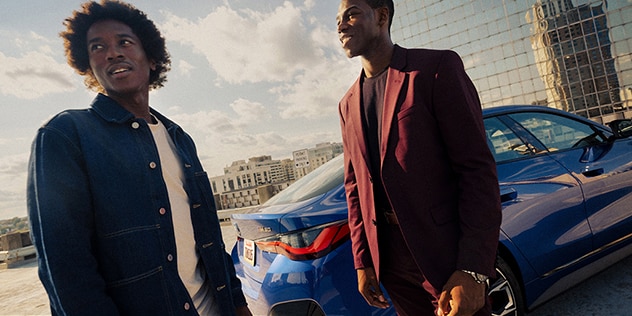 Two men converse near a parked BMW sedan in a city environment