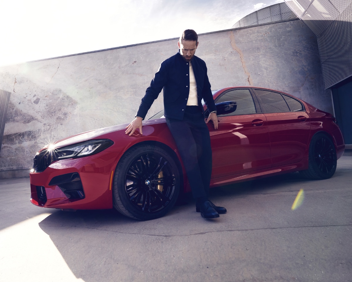 A man leaning against a BMW M5 in Imola Red
