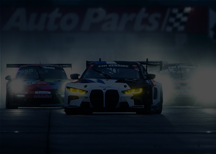 BMW race cars lead a crowded field of competitors on the track at dusk