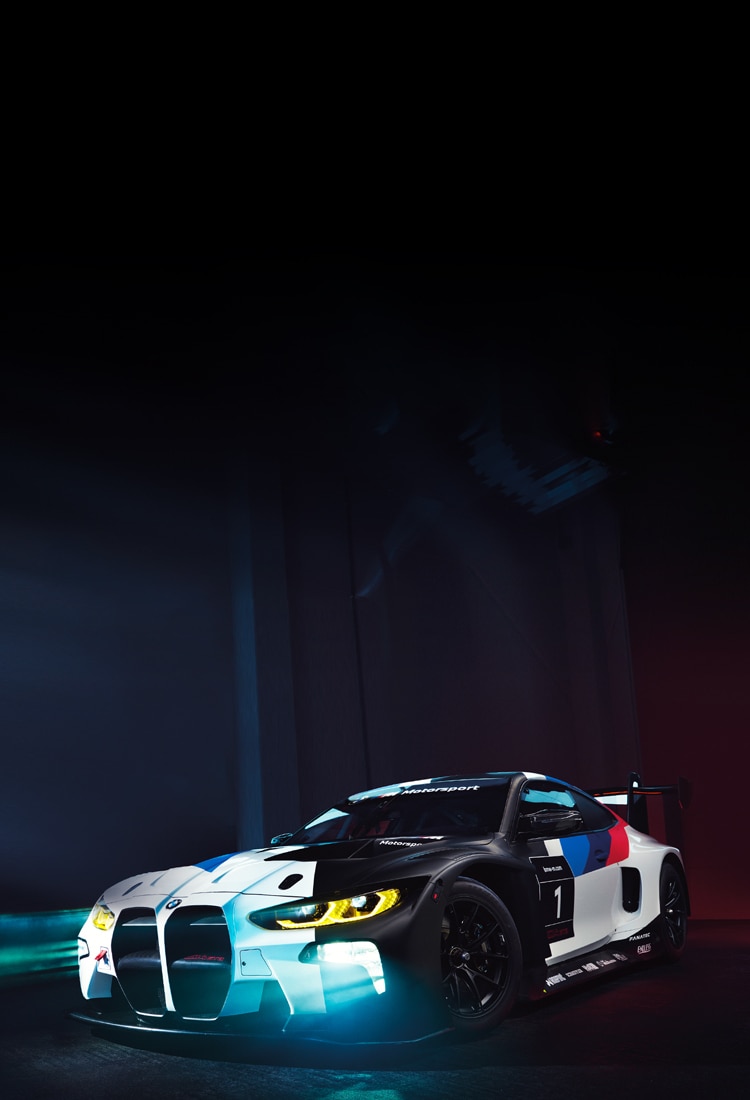 A BMW M4 GT3 in race livery with its lights on