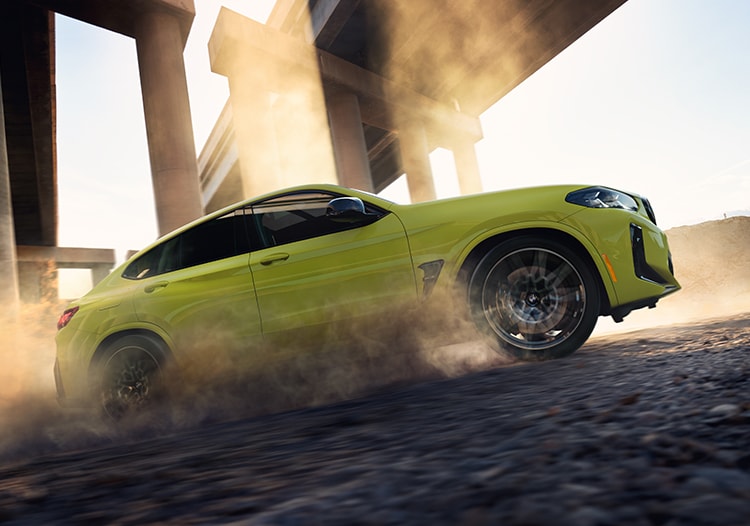 Side shot of the 2025 BMW X4 M in Sao Paolo Yellow driving on a dirt road