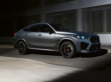 3/4 profile shot of the BMW X6 M Competition driving in an urban setting