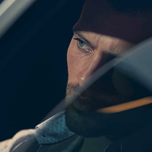 A driver looks out the window with his face partially shaded 