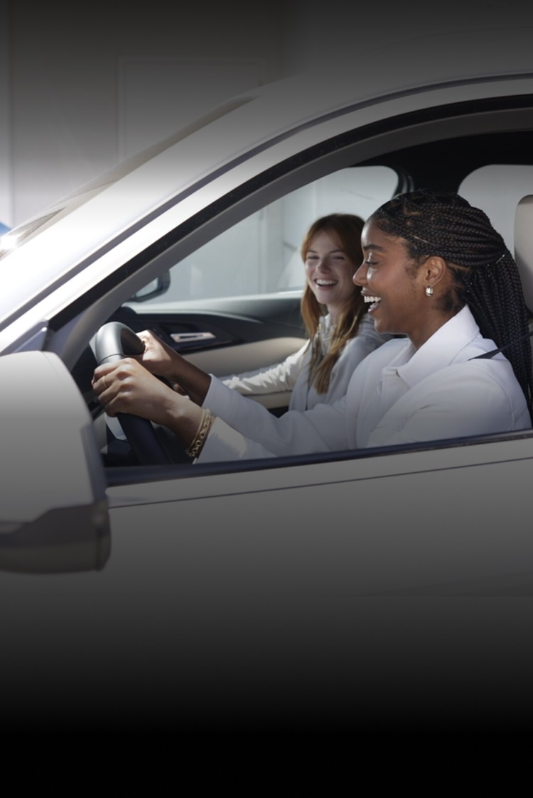 A driver and her passenger smile from the front seats of a BMW SUV.